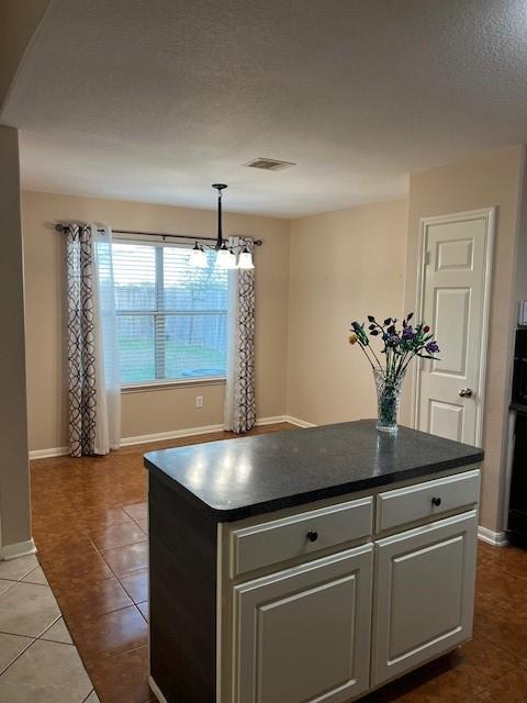 kitchen with a center island, dark countertops, visible vents, light tile patterned flooring, and baseboards