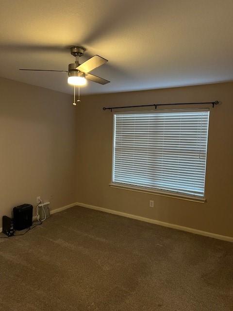 empty room with baseboards, dark colored carpet, and a ceiling fan