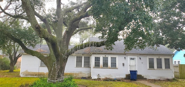 back of property with entry steps, a shingled roof, a yard, and fence