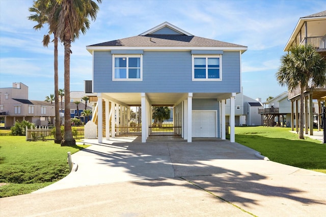 raised beach house with a shingled roof, concrete driveway, stairs, a front lawn, and a carport