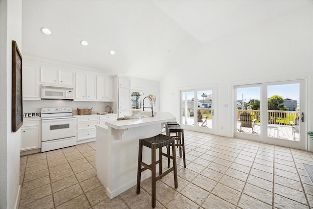 kitchen with white appliances, white cabinets, light countertops, a kitchen bar, and a center island with sink