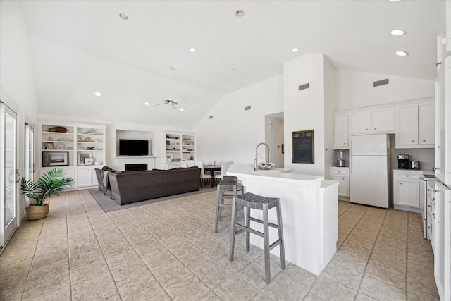 kitchen with a breakfast bar, a fireplace, freestanding refrigerator, white cabinets, and ceiling fan