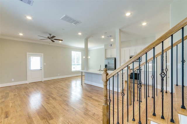 interior space featuring light wood-style flooring, visible vents, baseboards, stairs, and ornamental molding