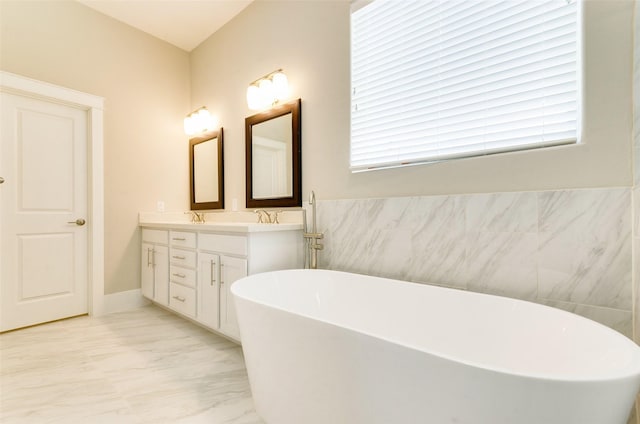 full bath with a freestanding bath, marble finish floor, double vanity, and a sink