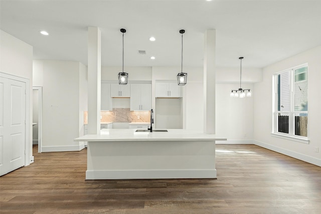 kitchen featuring backsplash, white cabinets, an island with sink, baseboards, and recessed lighting