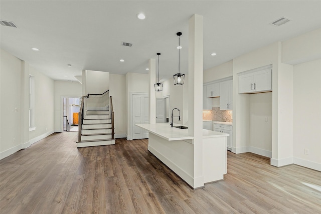 kitchen featuring wood finished floors, light countertops, an island with sink, baseboards, and a sink