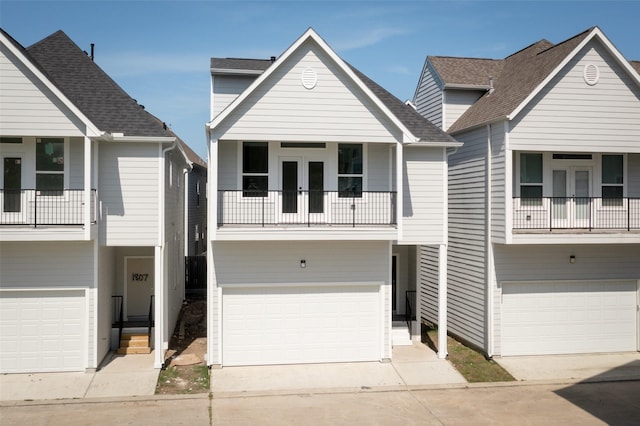 view of front of house with french doors, an attached garage, a balcony, and concrete driveway