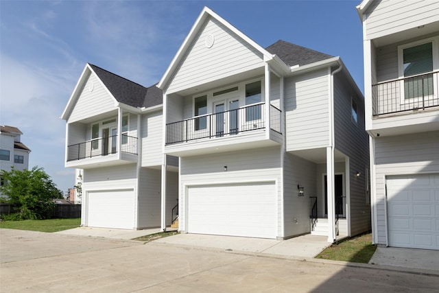 multi unit property with a balcony, an attached garage, a shingled roof, and concrete driveway
