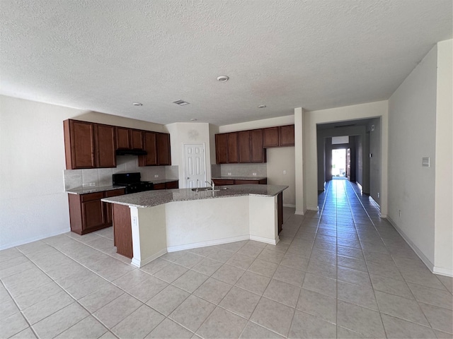 kitchen with tasteful backsplash, a kitchen island with sink, black range with gas cooktop, a sink, and light tile patterned flooring