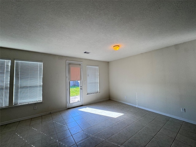 empty room featuring baseboards, visible vents, a textured ceiling, and tile patterned floors