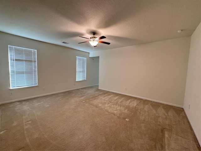 carpeted spare room featuring baseboards, ceiling fan, visible vents, and a textured ceiling