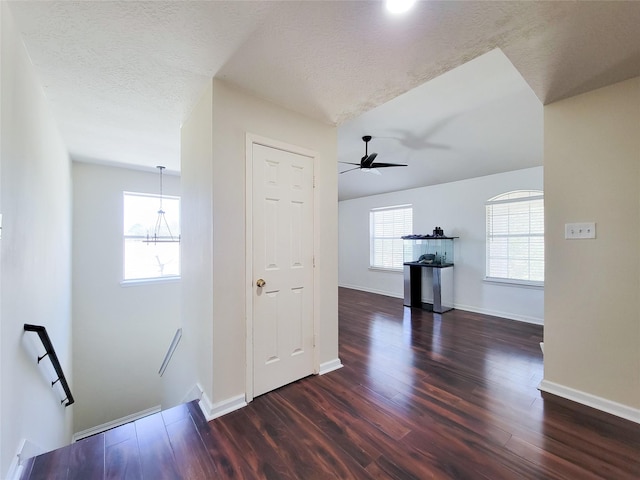 corridor with dark wood-type flooring, baseboards, a textured ceiling, and an upstairs landing