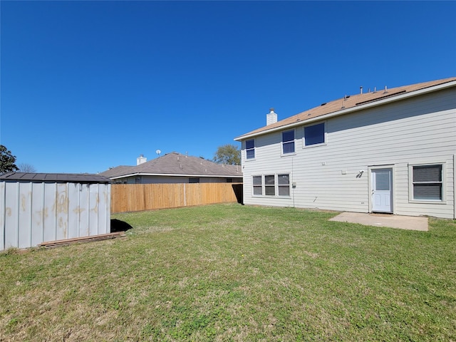 back of house featuring a yard, a chimney, a storage unit, fence, and an outdoor structure