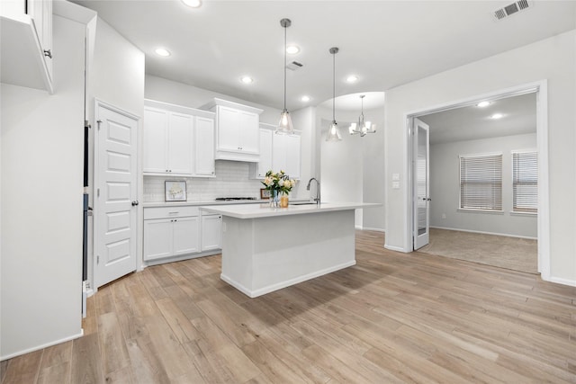 kitchen featuring light wood-style flooring, visible vents, white cabinets, light countertops, and decorative backsplash