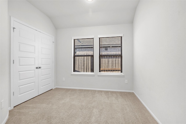 carpeted spare room featuring lofted ceiling and baseboards