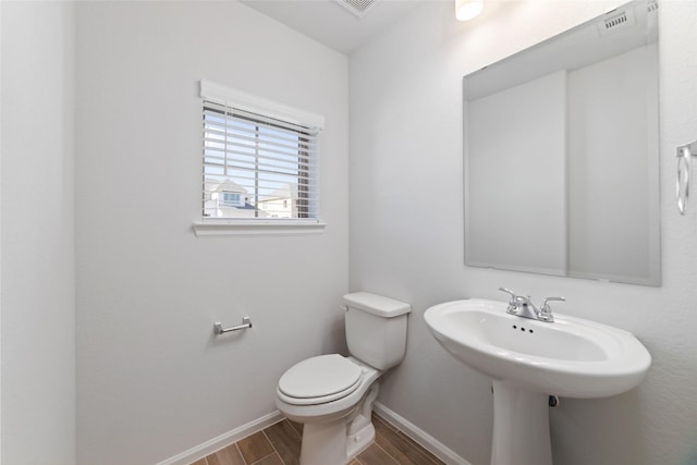 bathroom with toilet, a sink, visible vents, baseboards, and wood tiled floor