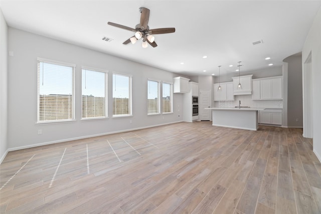 unfurnished living room featuring visible vents, a sink, and light wood-style flooring