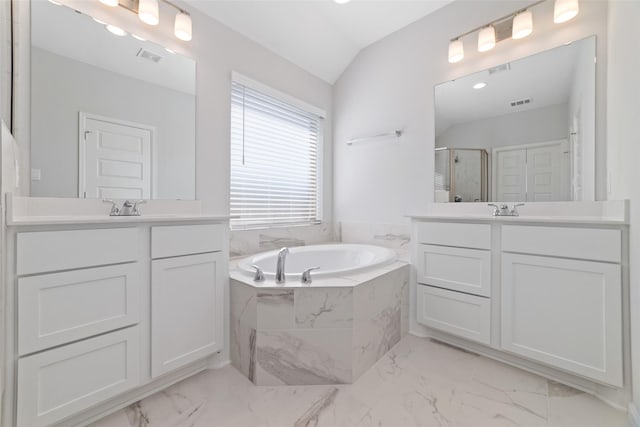 bathroom featuring a stall shower, vaulted ceiling, a garden tub, and two vanities