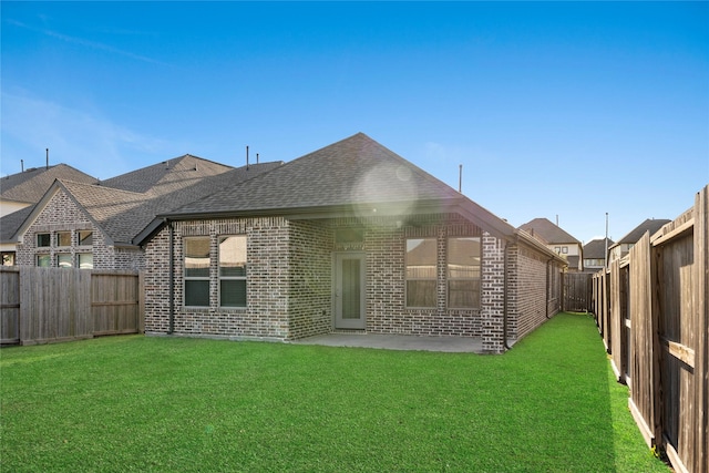 rear view of house with brick siding, a yard, a fenced backyard, and roof with shingles