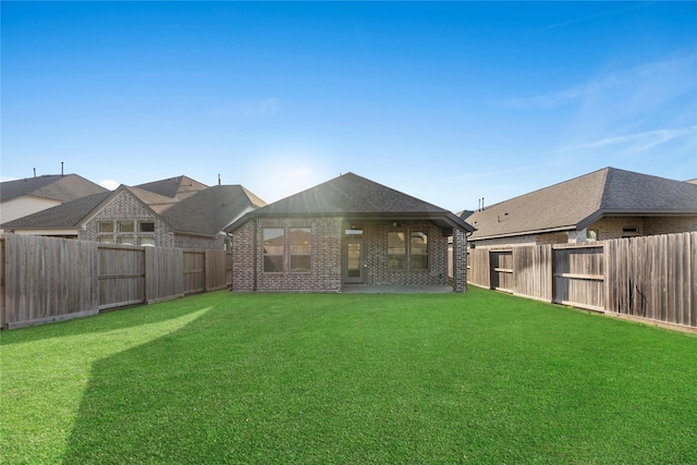 back of house with brick siding, a fenced backyard, roof with shingles, and a yard