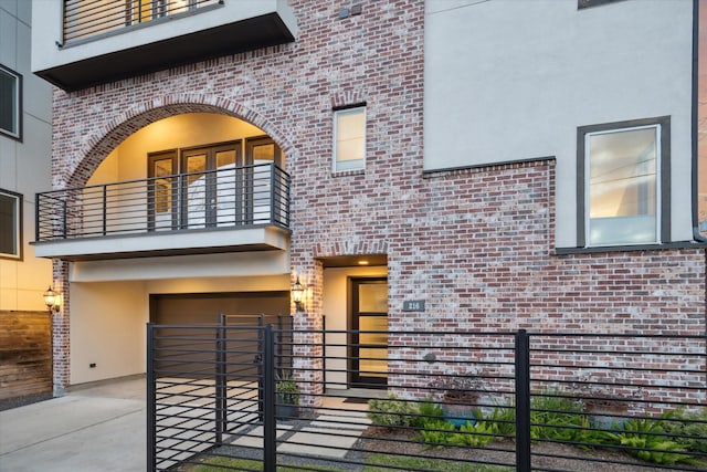 view of front of house featuring driveway, a balcony, an attached garage, fence, and brick siding