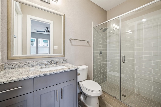 full bath with a textured wall, toilet, a ceiling fan, a stall shower, and vanity