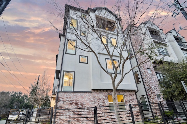 view of front facade with brick siding, fence, and stucco siding