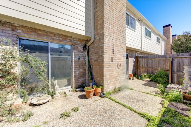 view of property exterior with a patio area, fence, and brick siding