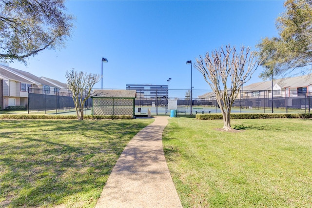 view of community with a tennis court, a residential view, fence, and a lawn