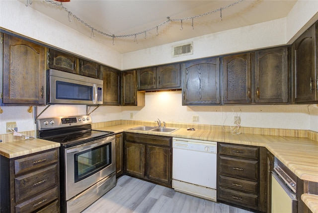 kitchen featuring visible vents, stainless steel appliances, dark brown cabinets, light countertops, and a sink