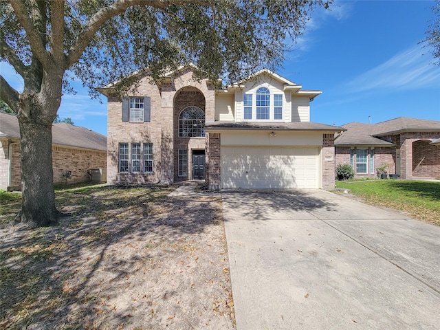 traditional-style house with brick siding, driveway, an attached garage, and central air condition unit