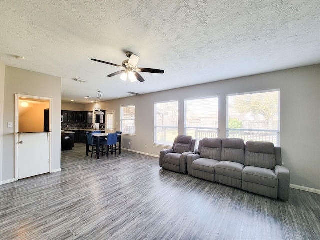 living room featuring ceiling fan, a textured ceiling, dark wood-style flooring, visible vents, and baseboards