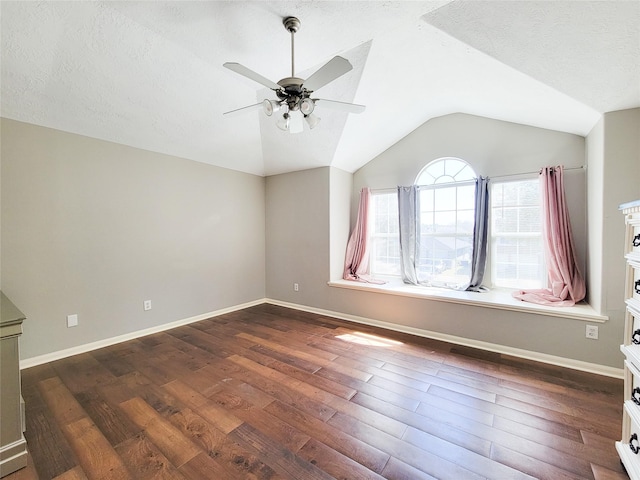 empty room featuring lofted ceiling, a textured ceiling, baseboards, and dark wood-type flooring