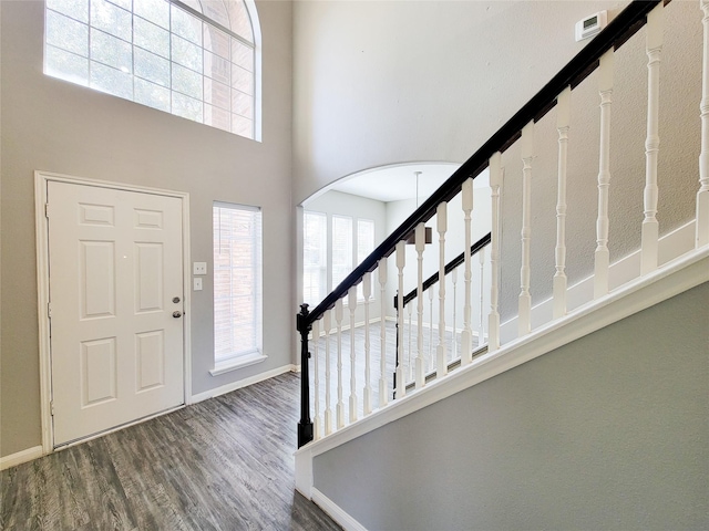 entryway with arched walkways, wood finished floors, a towering ceiling, baseboards, and stairway