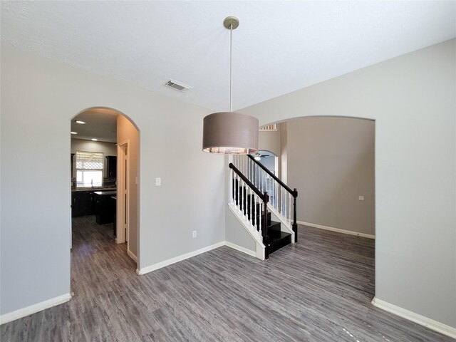 empty room with baseboards, visible vents, arched walkways, stairway, and wood finished floors