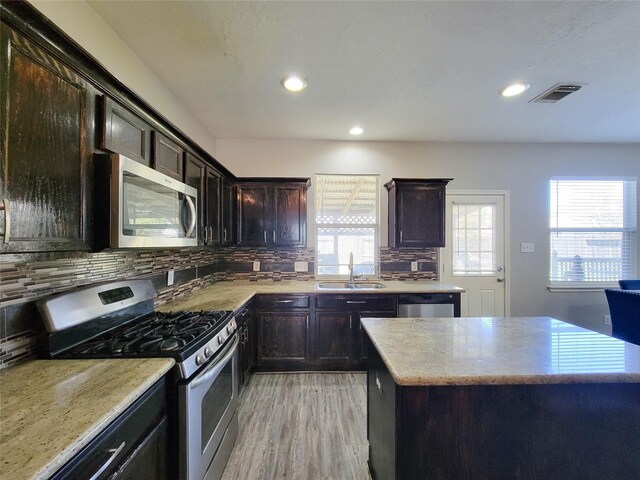 kitchen with a sink, visible vents, light wood-style floors, appliances with stainless steel finishes, and backsplash