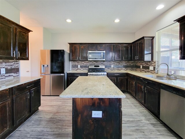 kitchen with appliances with stainless steel finishes, light wood-type flooring, a sink, and a center island