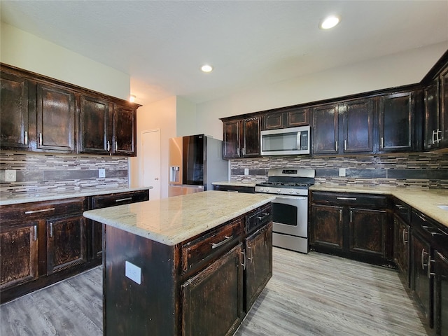 kitchen with appliances with stainless steel finishes, a kitchen island, light wood-style flooring, and decorative backsplash