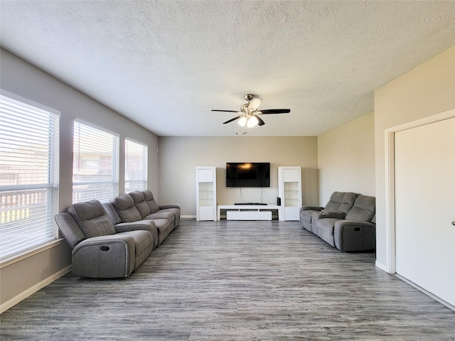 living area featuring a textured ceiling, wood finished floors, a ceiling fan, and baseboards