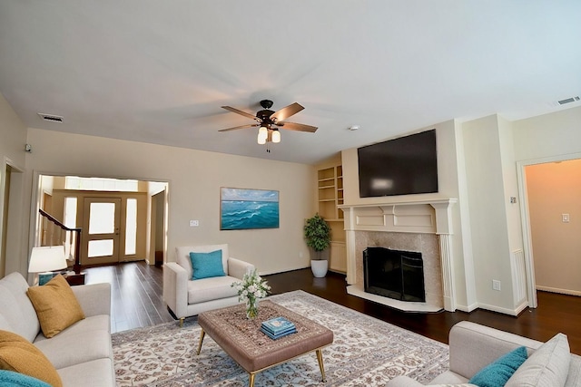 living room featuring a ceiling fan, a fireplace, visible vents, and wood finished floors