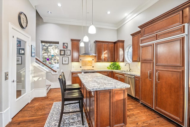 kitchen featuring a sink, appliances with stainless steel finishes, a center island, wall chimney exhaust hood, and dark wood finished floors