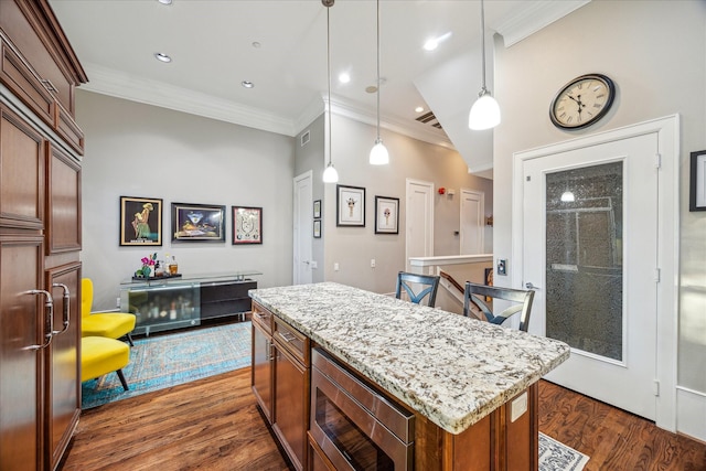 kitchen with dark wood-style floors, hanging light fixtures, stainless steel microwave, and a kitchen island