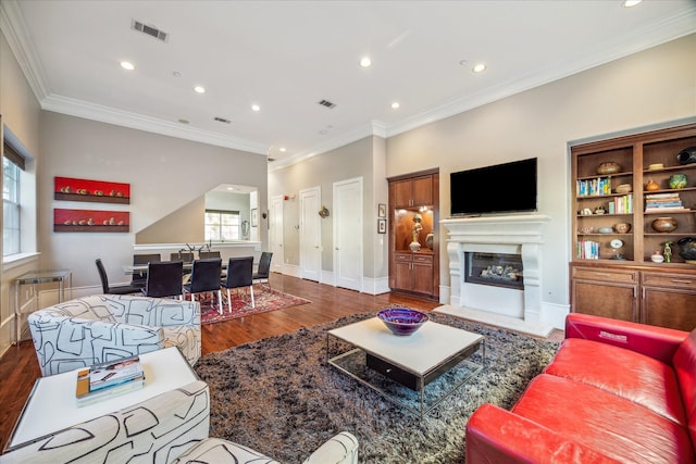 living room with ornamental molding, dark wood-type flooring, a glass covered fireplace, and visible vents