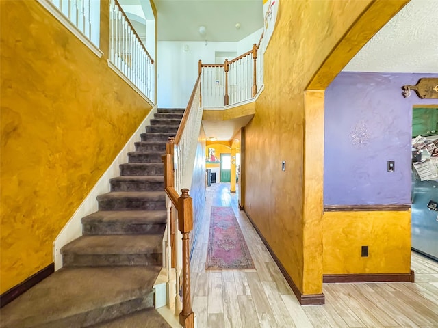 stairs featuring a high ceiling, wood finished floors, and baseboards