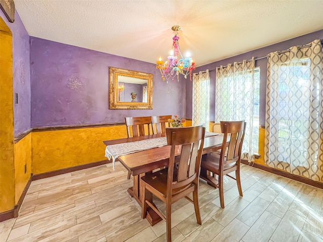 dining room featuring a wainscoted wall, a textured ceiling, wood finished floors, a chandelier, and baseboards