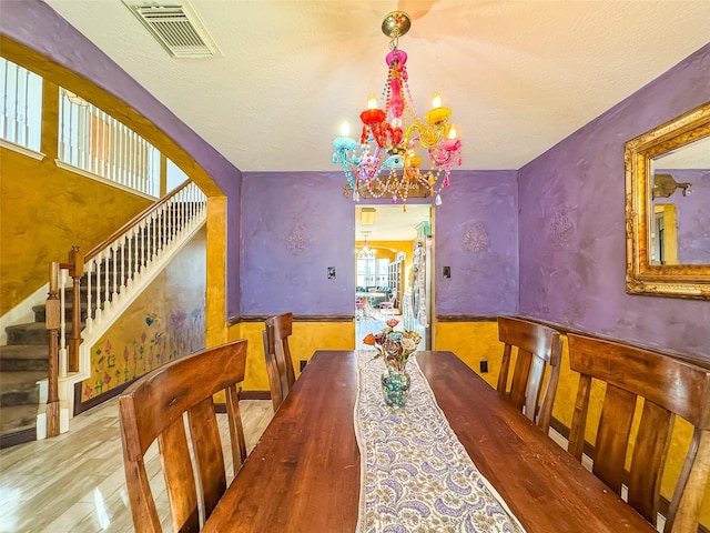 dining area featuring arched walkways, a wainscoted wall, a notable chandelier, visible vents, and stairway