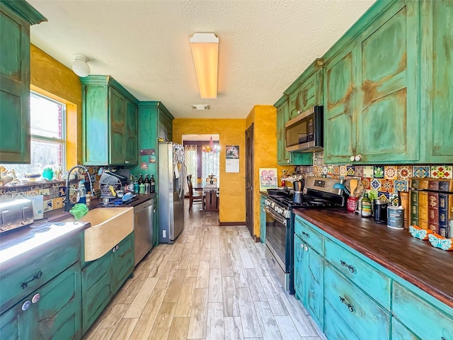 kitchen featuring decorative backsplash, appliances with stainless steel finishes, a textured ceiling, light wood-type flooring, and green cabinets