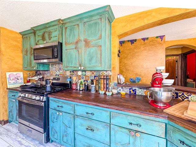 kitchen featuring appliances with stainless steel finishes, arched walkways, butcher block countertops, and a textured ceiling