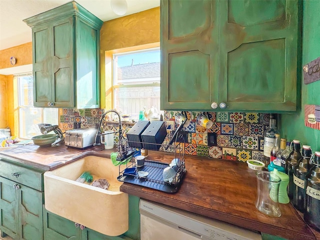 kitchen with dark countertops, green cabinetry, dishwasher, and backsplash