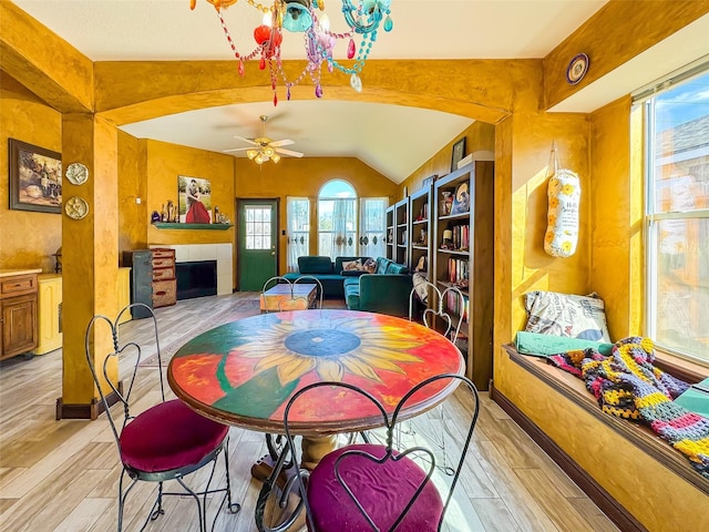 dining area featuring light wood-style floors, plenty of natural light, a fireplace, and vaulted ceiling